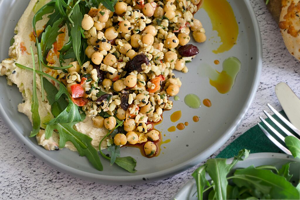 pexels-photo-30488354-30488354 Delicious Mediterranean salad with chickpeas, hummus, arugula, and olives, drizzled with olive oil.