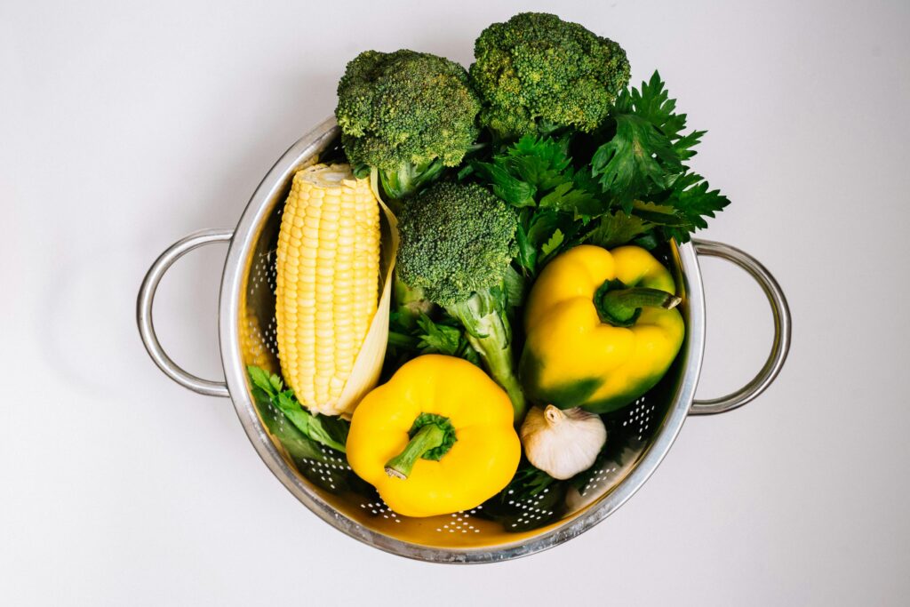 pexels-photo-5620892-5620892 Colorful vegetables including bell peppers, broccoli, corn, and garlic in a metal strainer, perfect for healthy cooking inspiration.
